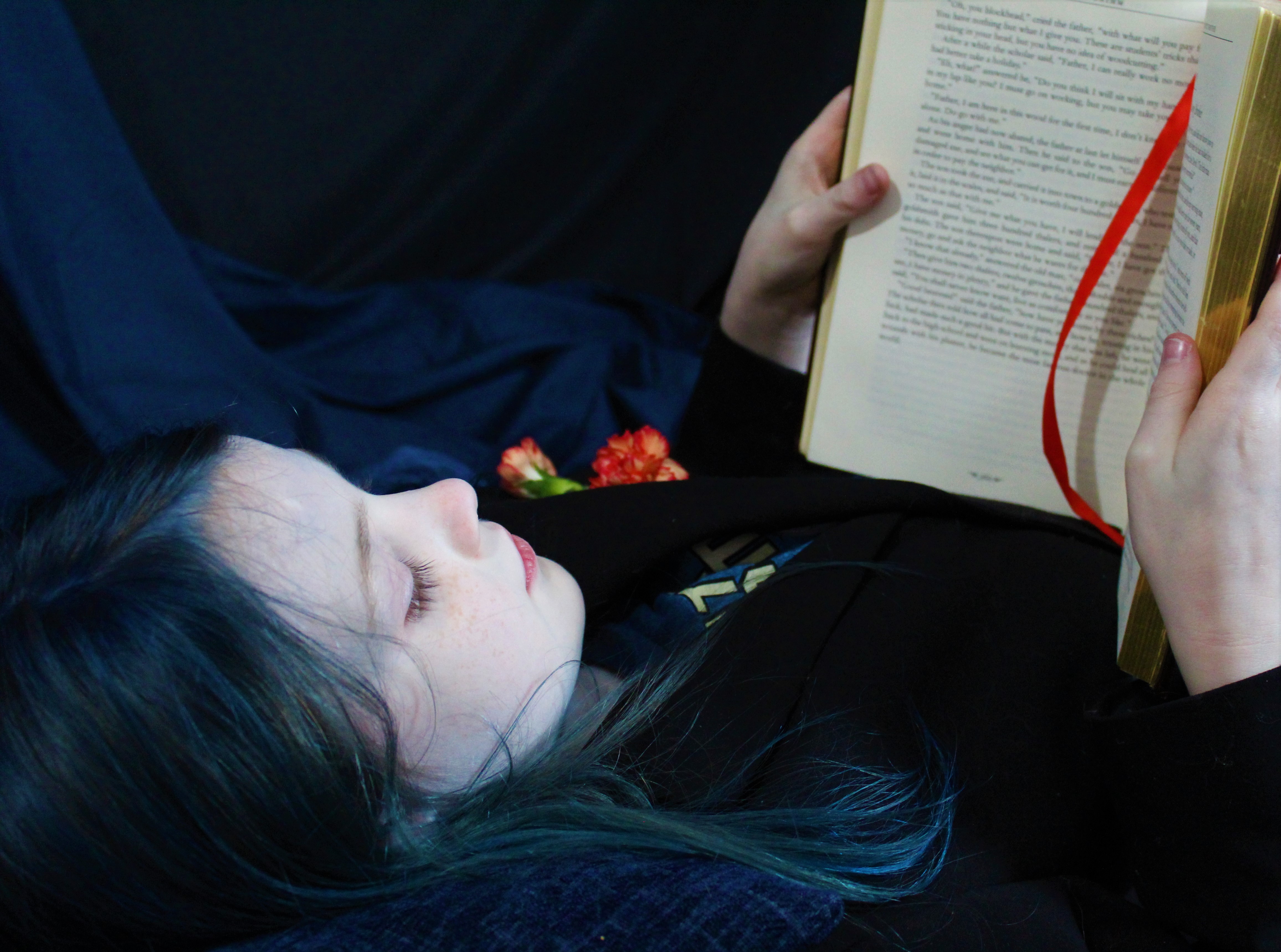 Close up of a boy with long, blue hair, reading a book.