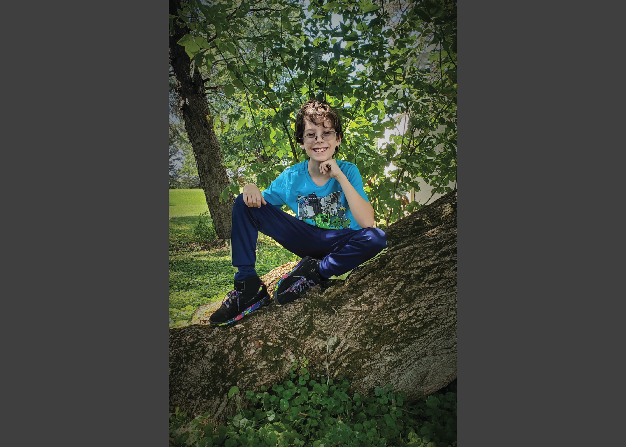 Portrait of a shorthaired brunette boy with glasses sitting on a falen tree outside.